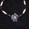 A hand-carved turtle from tagua nut inlaid with glow-in-the-dark powder and peacock opal on a bracelet with malachite, metal, bone, and wood beads