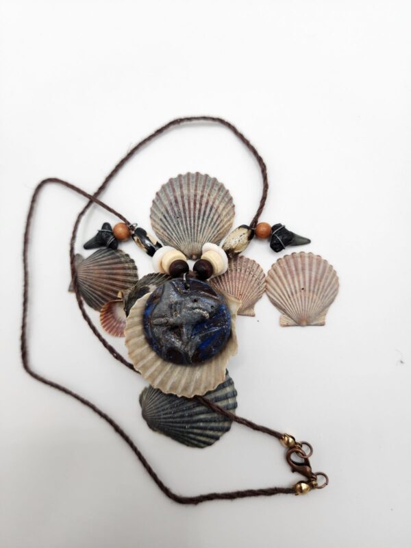 A shark carved into a coconut disc and painted gray as a pendant on a necklace with fossilized shark teeth, puka shells, and coconut beads