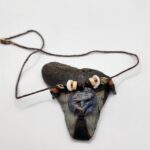 A shark carved into a coconut disc and painted gray as a pendant on a necklace with fossilized shark teeth, puka shells, and coconut beads